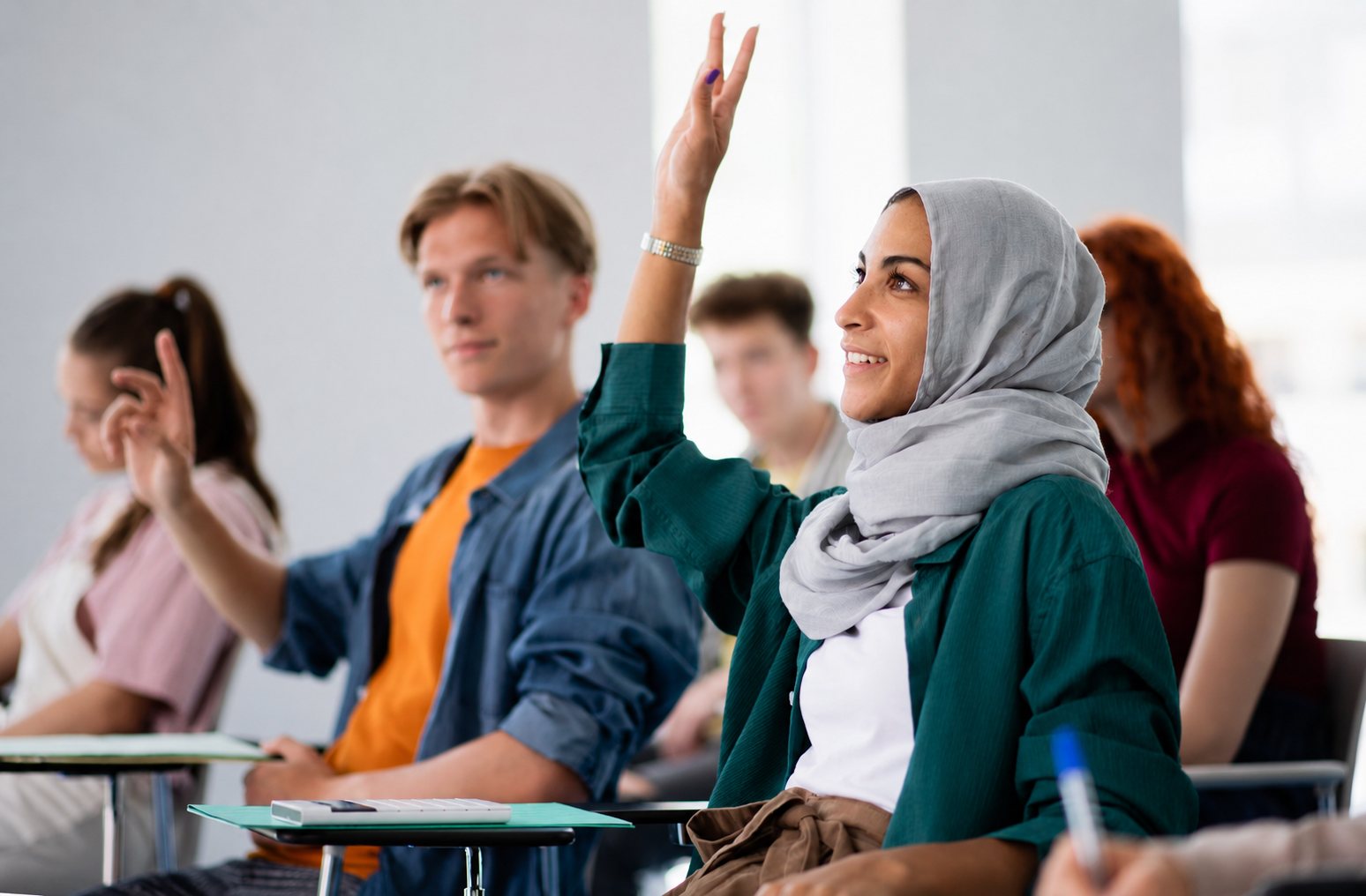 Een leerling steekt lachend haar hand op tijdens een workshop in de klas.