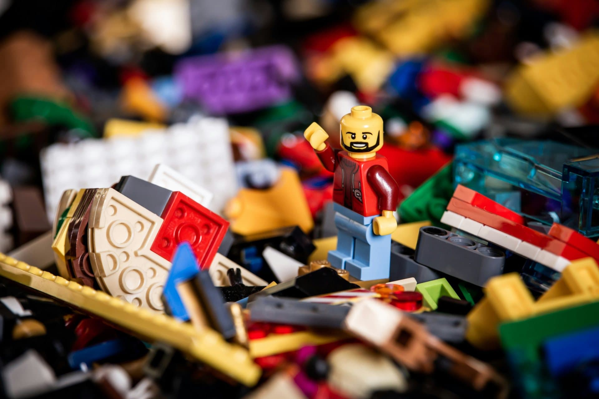 Een LEGO-poppetje zit bovenop een berg kleurrijke LEGO-stenen.