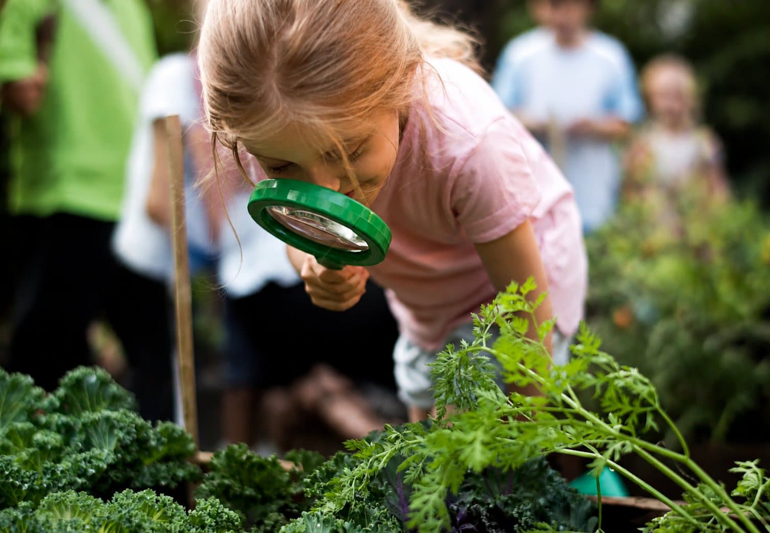 Een leerling bekijkt planten door een vergrootglas in de schooltuin.