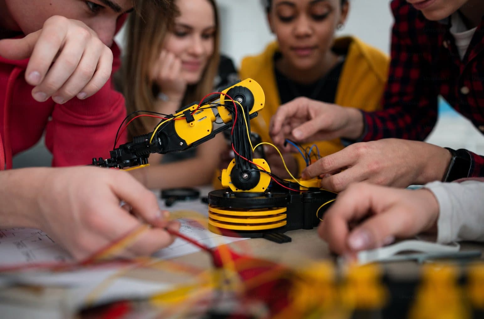 Leerlingen bouwen samen aan een gele robotarm op tafel.